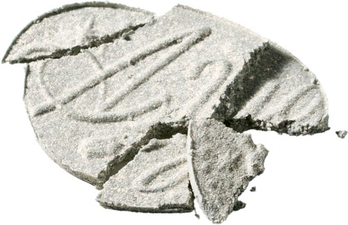 Trasiga delar av ett runt, platt föremål med en texturerad yta och mörka märken, möjligen en tablett eller skiva.