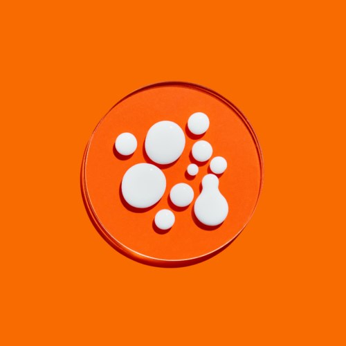 Weiße Pillen verschiedener Größen auf orangeem Hintergrund in einer transparenten runden Schale.