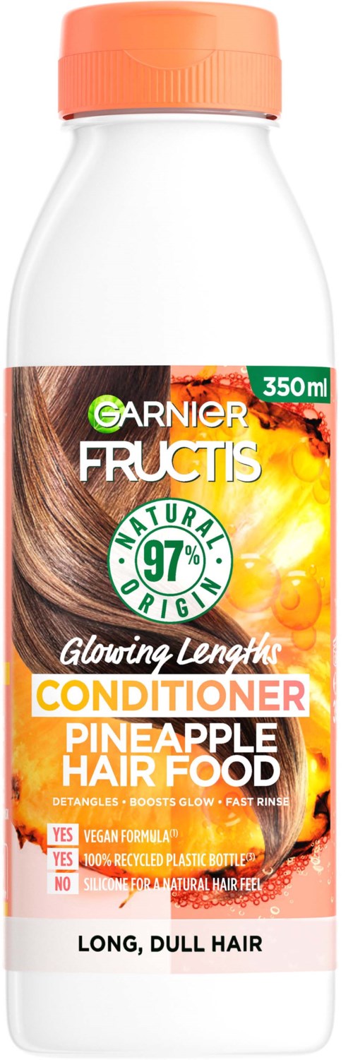 En vit flaska med orange lock, märkt Garnier Fructis balsam för matt, långt, matt hår med ananas hårmat.
