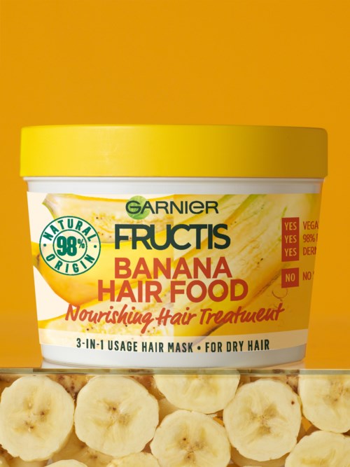 En burk Garnier Fructis Banana Hair Food för närande hår, passar för torrt hår, med bananskivor nedanför.