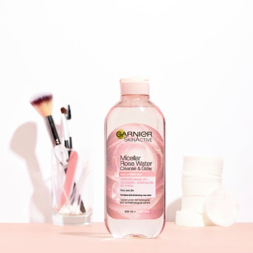 Een Garnier micellair waterfles in het midden, met wattenschijfjes rechts en make-up brushes links.