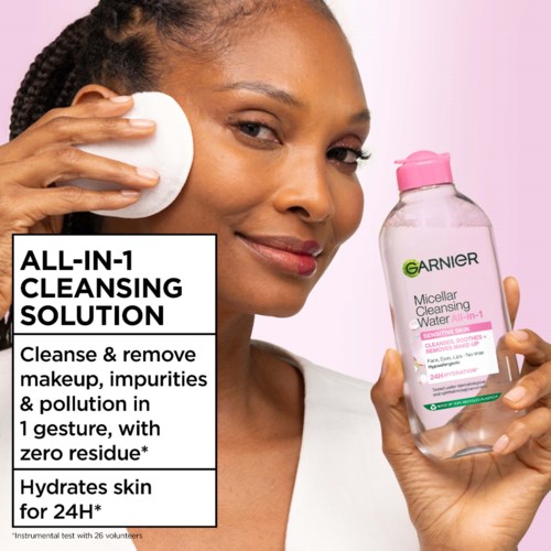 A woman uses a cotton pad to clean her face, holding Garnier micellar water for makeup removal.
