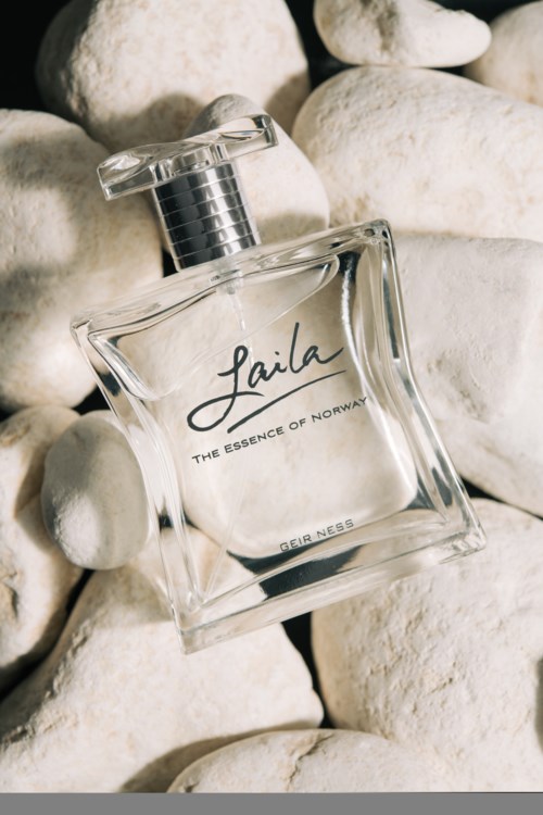 Een heldere parfumfles met zwarte dop op witte stenen, gelabeld 'Laila' en 'The Essence of Norway.'