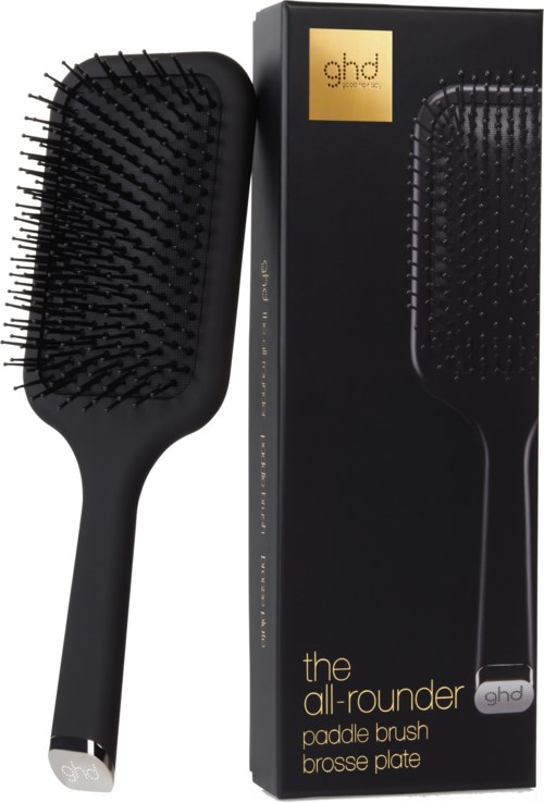 A black paddle brush with a long handle and wide bristles, next to its black box packaging with gold and white text.