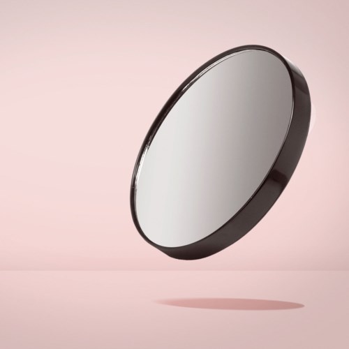Een ronde spiegel met een donkere rand, zwevend en werpt een schaduw op een roze achtergrond.