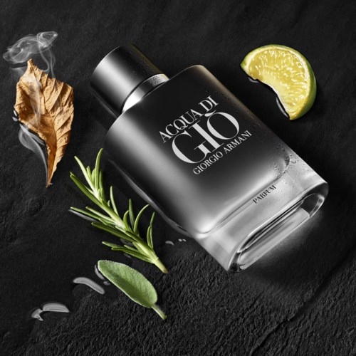 En Giorgio Armani-parfymflaska med lime, rosmarin, ett torrt löv och en citronklyfta på en svart yta.