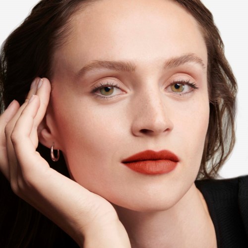 A woman with fair skin, brown hair, subtle makeup, and red lipstick looks calmly at the camera.
