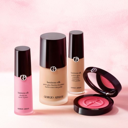 Three bottles of Giorgio Armani luminous silk foundation and a blush compact are displayed on a pink background.