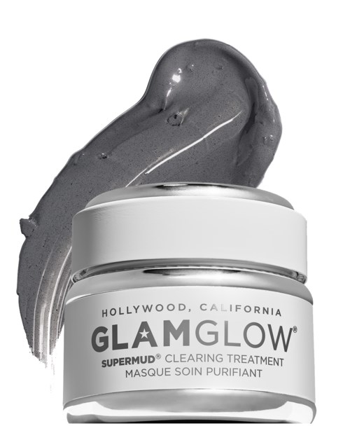 Et glassmerke med 'Glam Glow Supermud' og grå leiremaske bak den.
