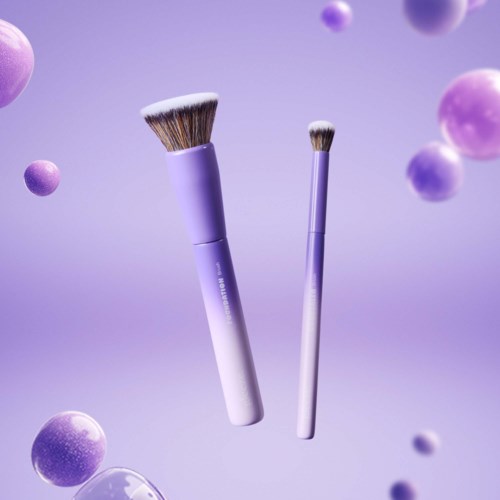 Två makeup-borstar flyter bland lila och rosa sfärer, med en mjuk lila bakgrund.
