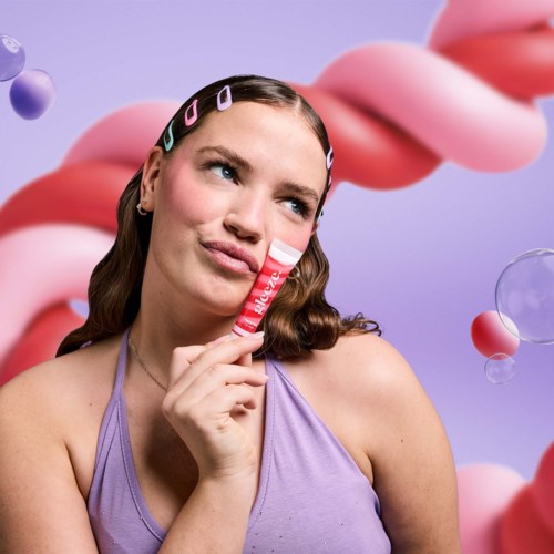 Een vrouw met haarclips, houdt een kleine tube bij haar gezicht, tegen een kleurrijke abstracte achtergrond.