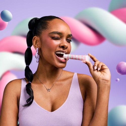Jonge vrouw met vlechten die lippenbalsem aanbrengt in een kleurrijke, speelse achtergrond.