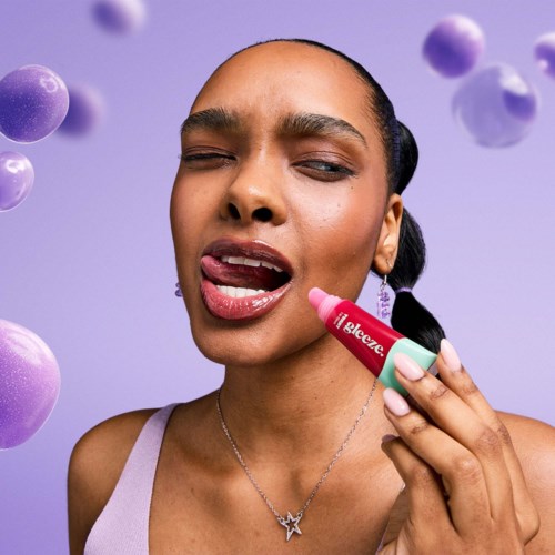 Eine Frau mit geschlossenen Augen trägt Lipgloss auf, umgeben von schwebenden lila Kugeln vor einem lila Hintergrund.