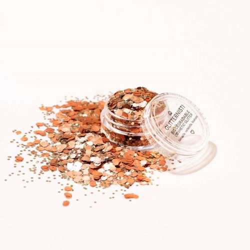Klein bakje glitter met oranje en zilveren glanzende stukjes die ernaast zijn gemorst.