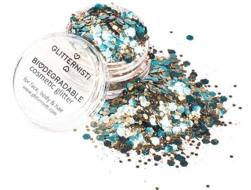 Een kleine container morst kleurrijke glitter op een oppervlak, met blauwe, gouden en witte stukjes eromheen.