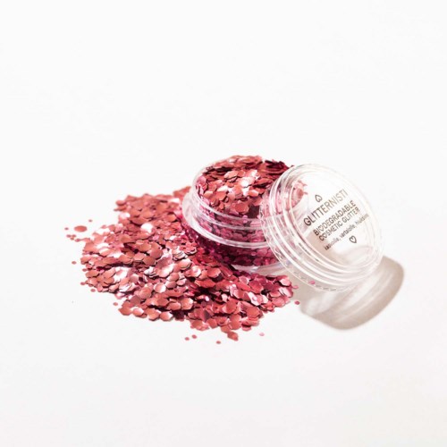Een ronde open container met roze glitter die over een witte achtergrond spat.