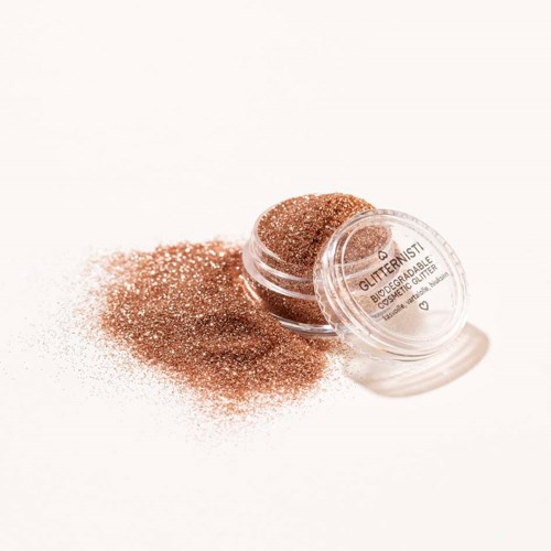 Een container met glinsterende bronzer en wat uitgegoten poeder op een witte ondergrond.