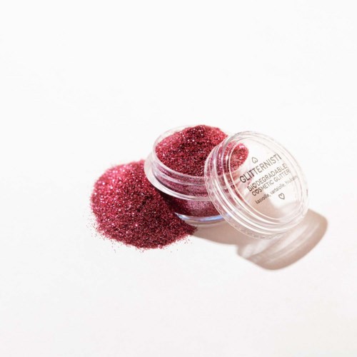 Een kleine ronde container gevuld met roze glitter, waarvan wat is uitgegoten op een witte achtergrond.