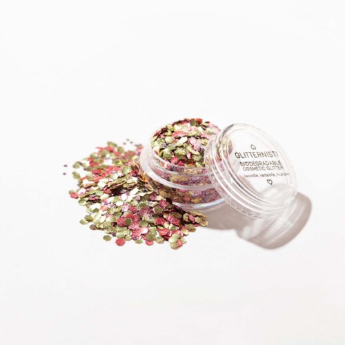 Kleurrijk glitter in een klein potje met wat ernaast op een witte ondergrond ligt.