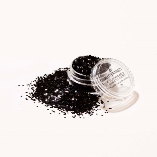 Een kleine ronde container gevuld met zwarte glitter, er ligt wat uitgegoten op een witte ondergrond.
