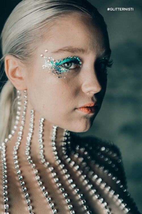 Een vrouw met glanzende make-up en parelversieringen op haar gezicht en nek, kijkt zijwaarts.