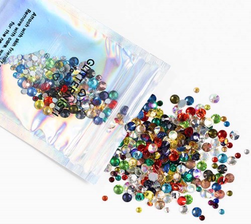 Kleurige strass-steentjes verspreid uit een verzegelde plasticzak op een witte ondergrond.