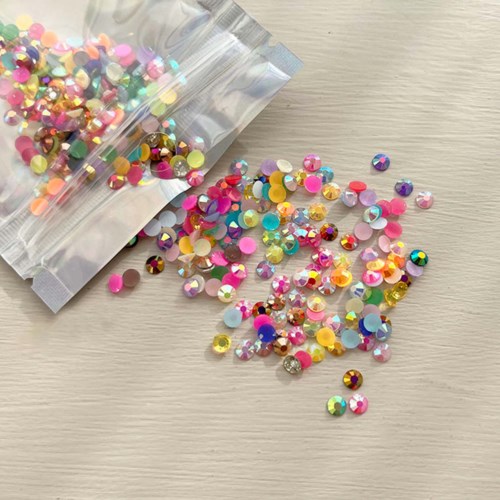 Kleurrijke ronde rhinestones vallen uit een plastic zak op een lichte ondergrond.