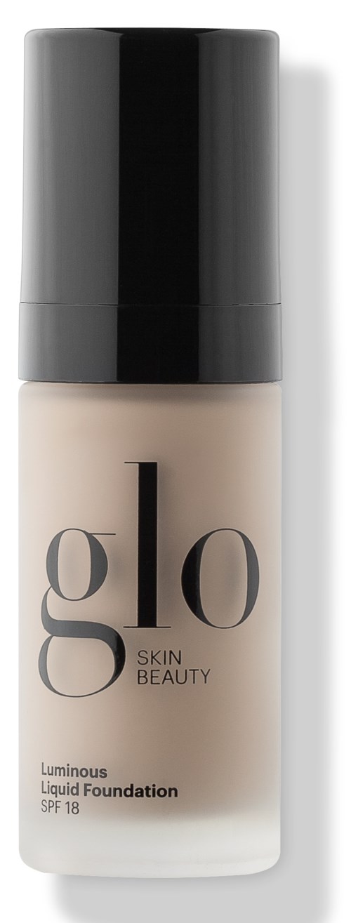 A bottle of Glo Skin Beauty luminous liquid foundation with SPF 18, black cap, and beige base.