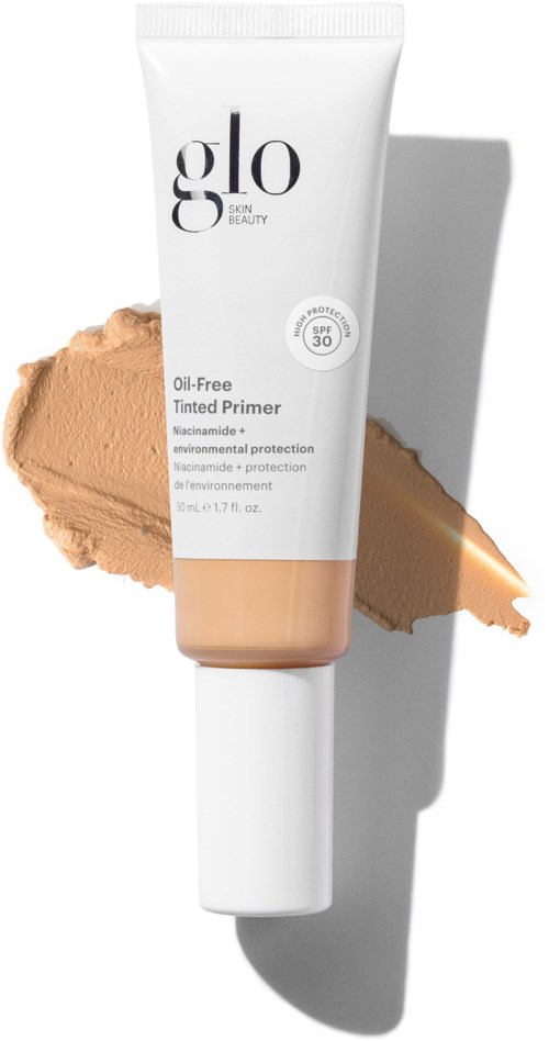 Eine weiße Tube mit Glo skin beauty Primer mit SPF 30 vor einem beige Make-up. Schatten rechts.