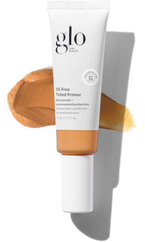 A white tube labeled Glo Tinted Primer with SPF 30, placed on a beige background, casting a shadow.