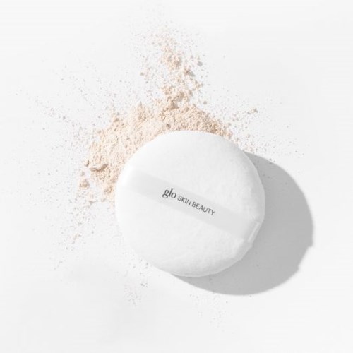 A white round beauty product with the label 'glo SKIN BEAUTY' on a light background, with loose powder nearby.