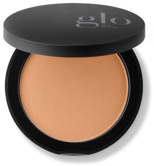 A compact of pressed powder with a black lid marked "glo BEAUTY". The powder is light beige.