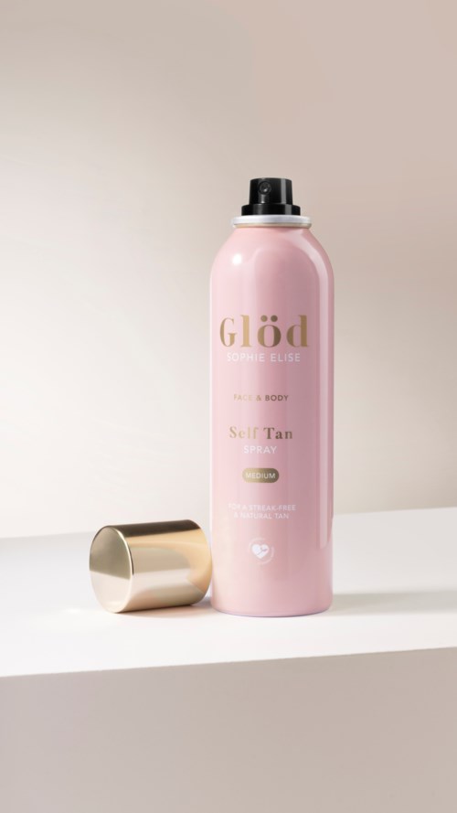 Pink bottle labeled Glöd Self Tan Spray with a gold cap on a white surface.