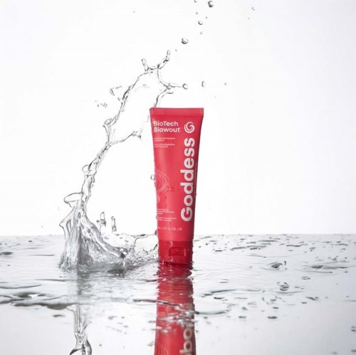 Een rode tube met 'Goddess' erop, staat in water met spatwater eromheen.