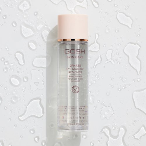 Een doorzichtige fles met roze deksel, gemerkt GOSH SKIN CARE 2PHASE EYE MAKEUP REMOVER, op een nat oppervlak.