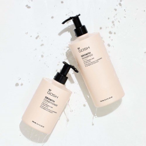 Twee flessen haarverzorgingsproducten, shampoo en conditioner, liggen op een wit oppervlak. Waterdruppels zijn in de buurt.