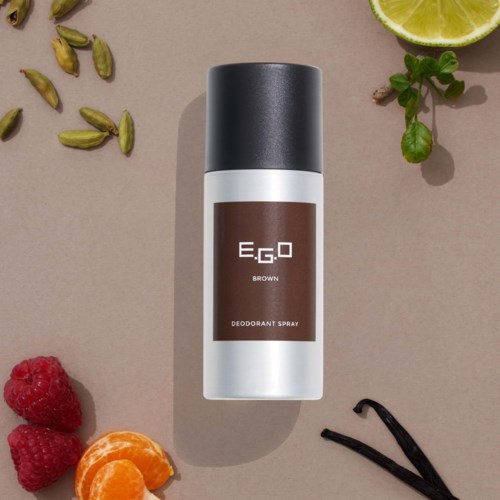 Deodorantspray met zwarte dop, gelabeld E.G.O BROWN, geplaatst op een beige oppervlak met limoen, bessen, kardemom en vanille.