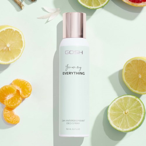 Eine weiße Deospray-Flasche mit roségoldener Kappe, umgeben von Zitronen- und Limettenscheiben auf pastellfarbenem Hintergrund.