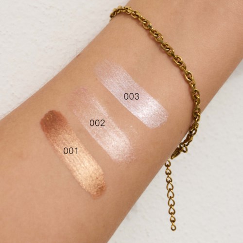 Three swatches of makeup shades on a person's arm, labeled 001, 002, 003, with a gold chain bracelet.