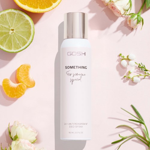 Een witte sprayfles met GOSH Something op een roze achtergrond, omringd door bloemen en citrusvruchten.