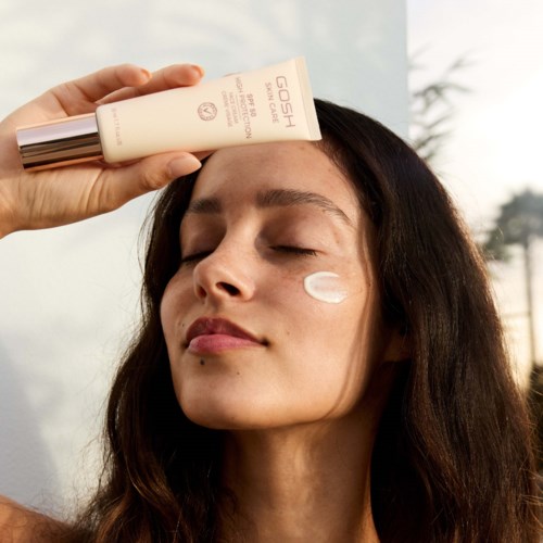 Een vrouw brengt lotion aan onder haar oog, houdt een tube met het label 'GOSH' tegen haar gezicht buiten.