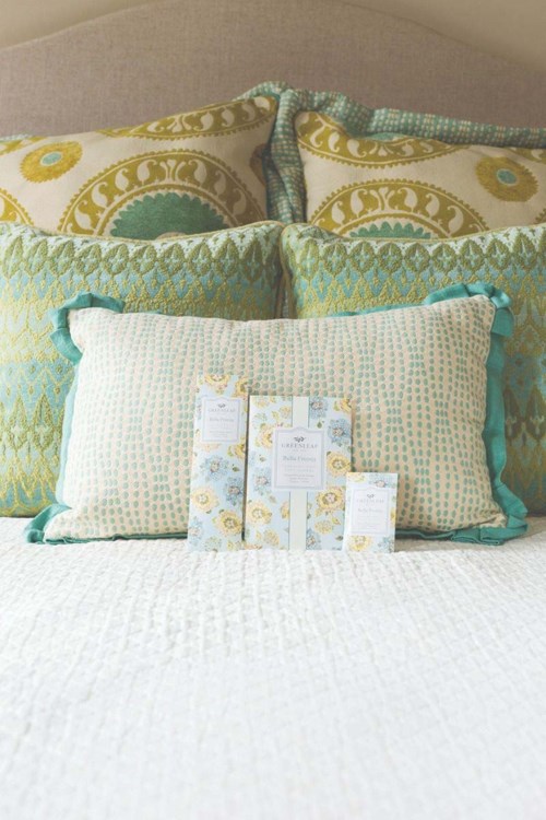 A bed with decorative pillows in pastel colors and patterned designs, with wrapped gifts in front.