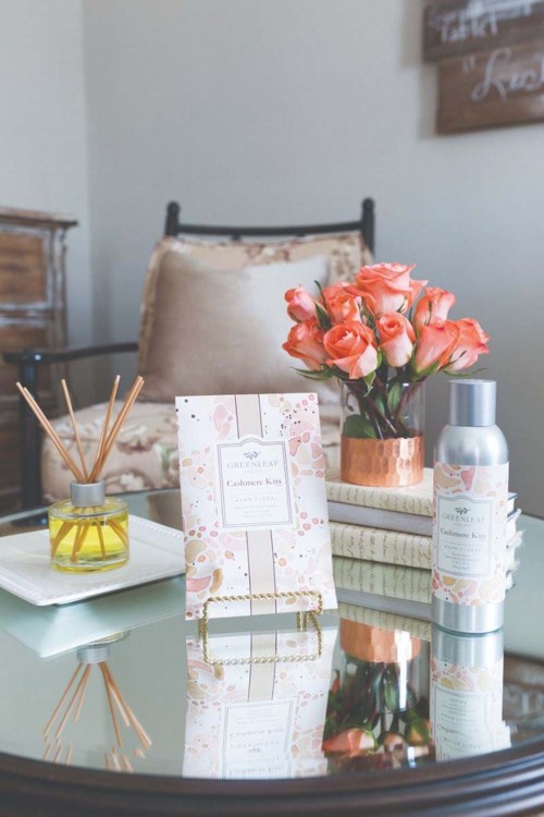 A table with a bouquet of pink roses, a candle, and some books, in a cozy room.