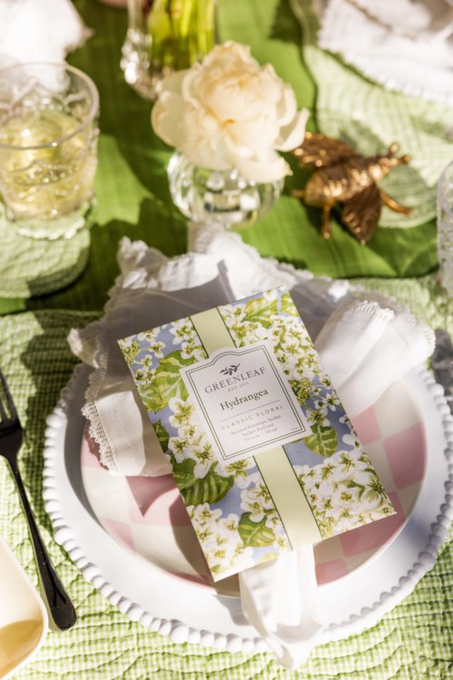 A table setting with a soap package, flowers, candles, and a butterfly decoration on a green cloth. Elegant and natural theme.