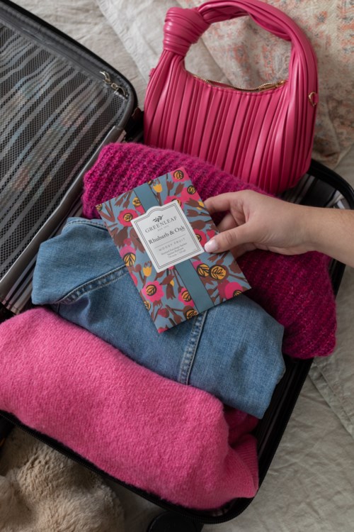 A suitcase contains clothes, a pink bag, and a book with colorful cover. The clothes include pink and blue fabrics.
