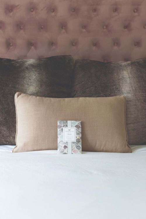 A beige pillow and a card on a bed with a dark headboard in the background.