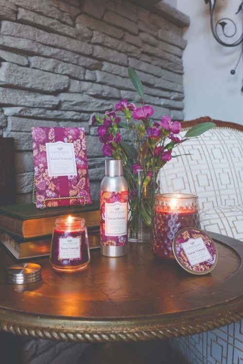 A table with candles, a bottle, flowers, and wrapped products in a cozy setting.