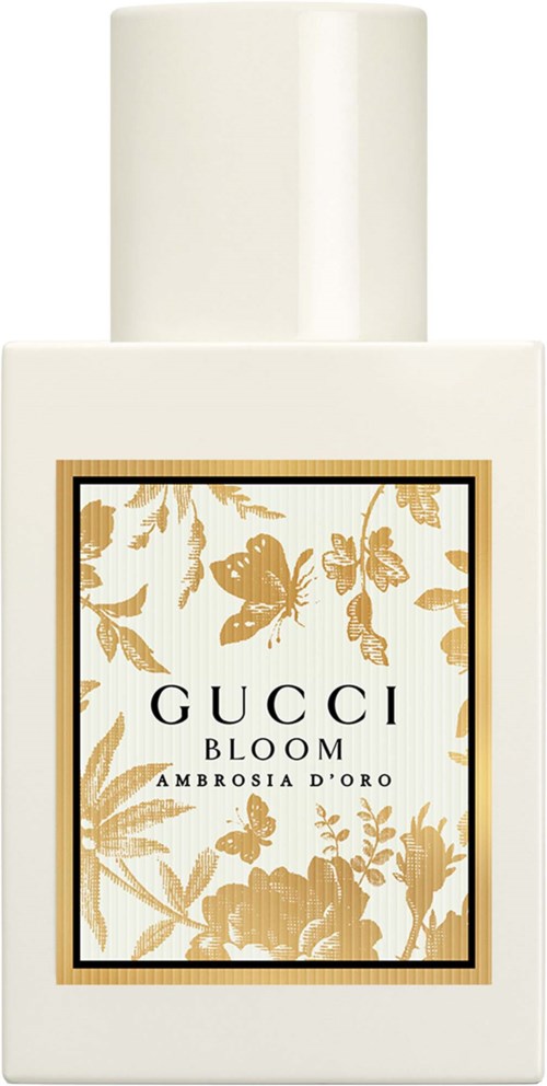 Een witte fles met een label met vlinders en bloemen in goudtinten, gemarkeerd Gucci Bloom Ambrosia D'Oro.