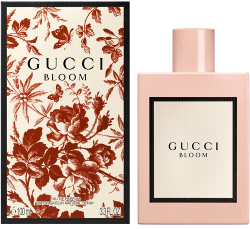 Een roze parfumfles met een lichte etiket en zwarte rand, naast een decoratieve doos met rode bloemen en zwarte rand.