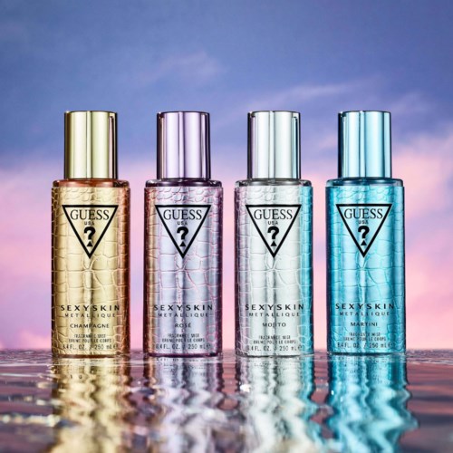 Vier GUESS-flessen in verschillende kleuren staan op water, reflecterend de lucht, tegen een zonsondergang.